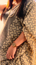 Woman in off-white and grey patterned saree, wearing beaded necklace and gold wristwatch