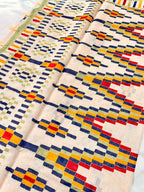 Cream-colored fabric with geometric multicolor embroidery, including red, blue, yellow, and green patterns
