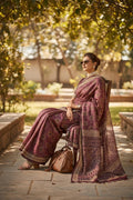 Woman in elegant maroon patterned saree with sunglasses, sitting outdoors in sunlight