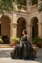 Woman in elegant black and gold saree sitting outdoors in a heritage courtyard