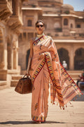 Woman in peach handloom saree with geometric patterns, walking outdoors with a leather bag